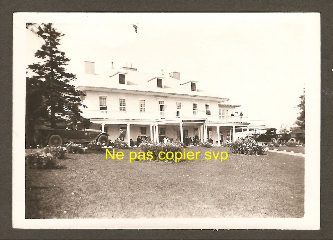 Photo de petites dimensions (8,9 x 6,2 cm) illustrant l'hôtel Kent House, au cours des années 1920. On remarque une automobile d'époque stationnée devant l'établissement, ainsi que quelques autres, plus en retrait, à droite.